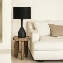 Load image into Gallery viewer, Corella tall black mango wood table lamp base with a black linen fabric drum lamp shade on a side table in a living room.
