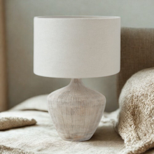 Load image into Gallery viewer, White washed ribbed wood table lamp base with a cream linen shade on a side table in a boho minimalist bedroom interior.