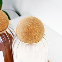 Load image into Gallery viewer, Two glass bottles with cork lids on a white background
