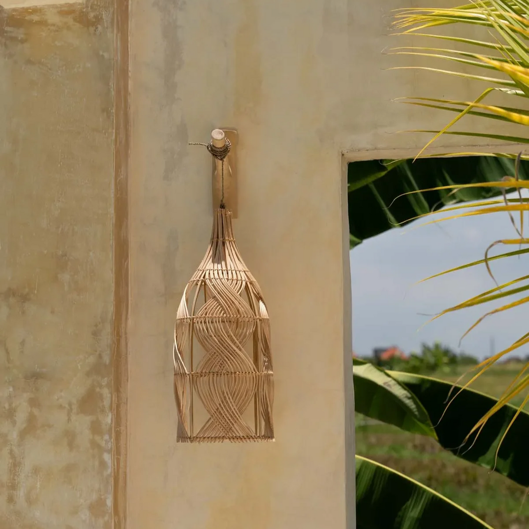 A natural woven pendant light shade hanging in front of a stone wall